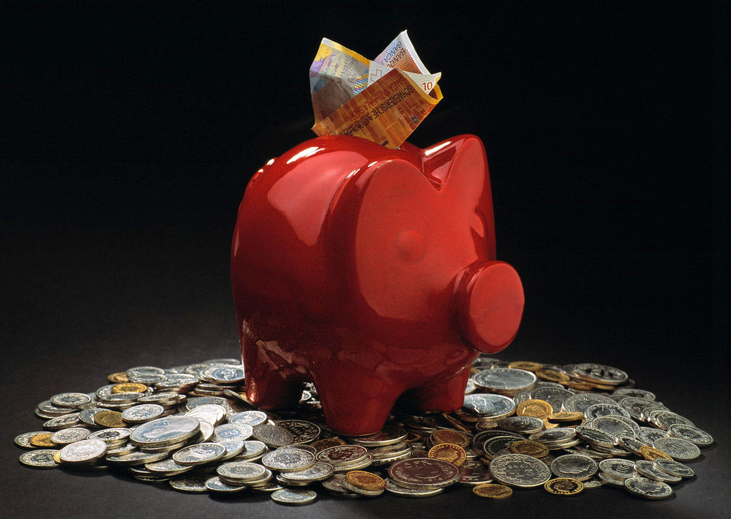 A red piggybank with notes sticking from the top sits on a pile of coins