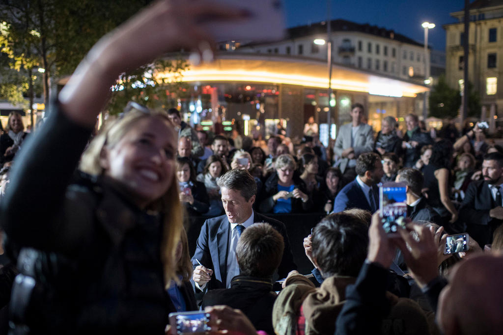 Hugh Grant gibt Autogramme, im Vordergrund eine Frau, die ein Selfie macht