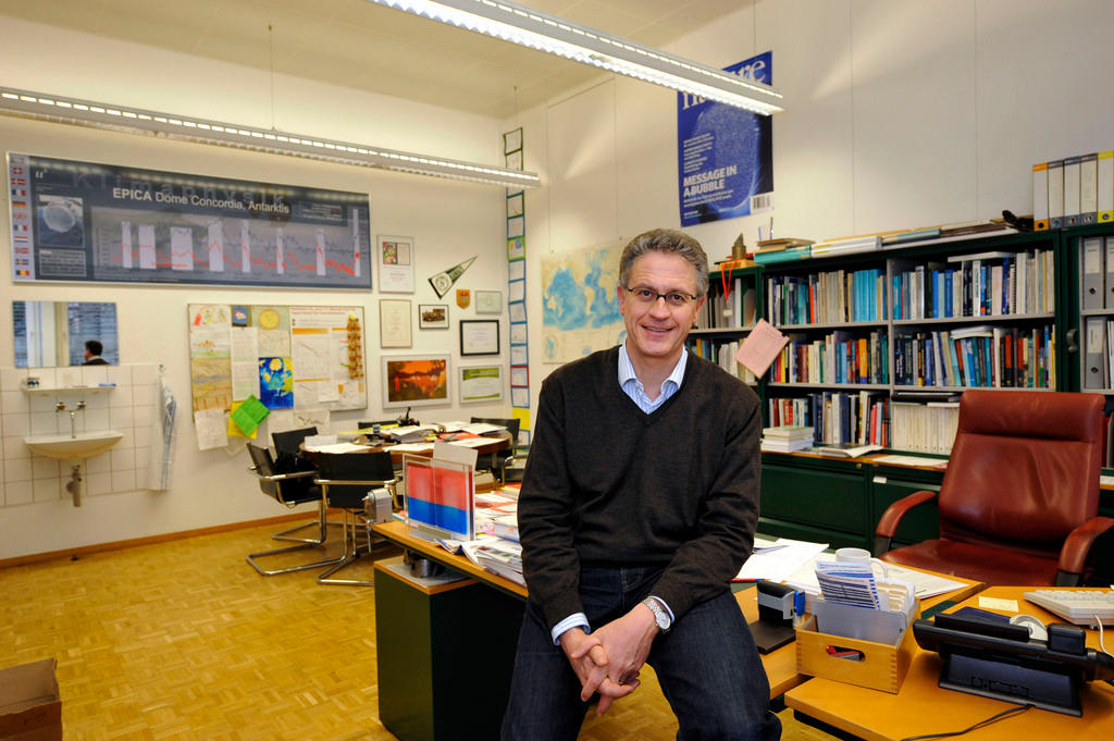 A smiling Thomas Stocker sits on his desk in his office