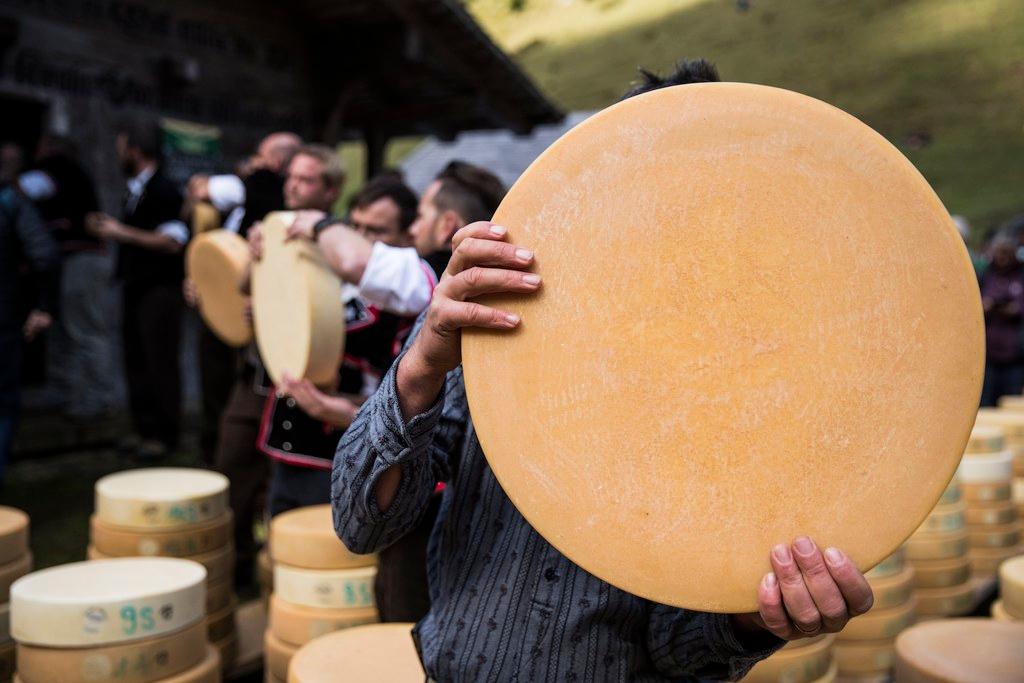 Una persona tiene in mano una grande forma di formaggio che nasconde tutta la sua faccia.