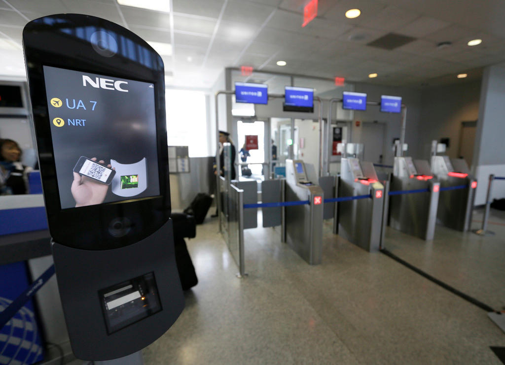 A flat screen, next to passport control booths, displays NEC