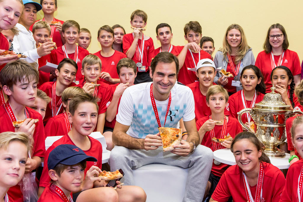 Roger Federer surrounded by pizza-eating ball boys and girls