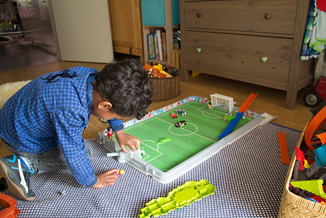 Ein Junge spielt auf dem Boden mit Fussballspielern aus Plastik.