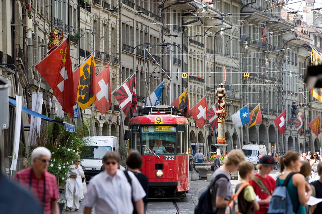A tram heads down a crowded Bern street against a backdrop of cantonal flags