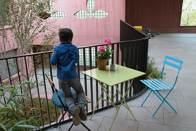 Ein Junge kniet auf einem Stuhl in einem Innenhof und schaut über das Geländer.