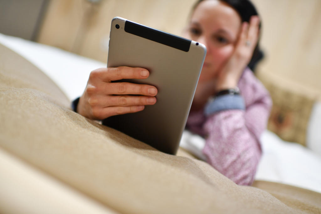 woman lying on bed with tablet