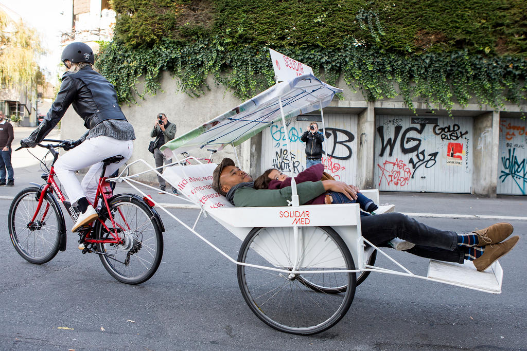 Eine Frau fährt auf einem roten Fahrrad mit Anhänger auf einer Strasse.