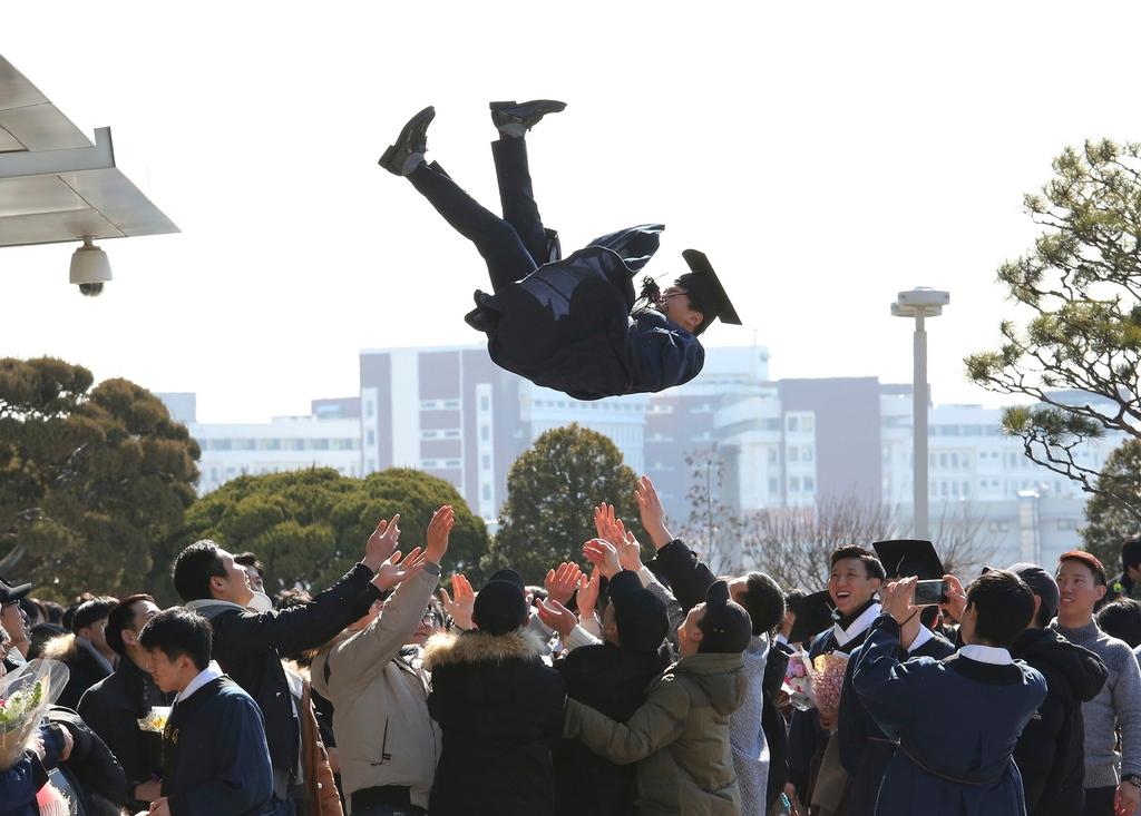 A student in robes and mortar board is thrown up in the air by colleagues