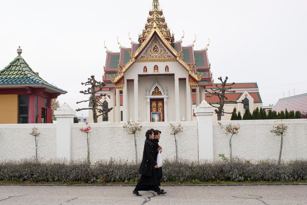 две женщины идут вдоль ограды тайского храма
