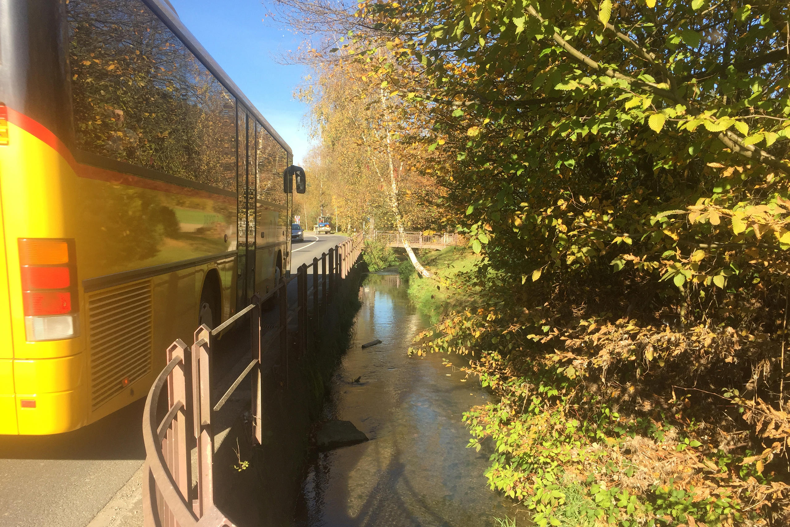 Ein Postauto fährt an Bach vorbei