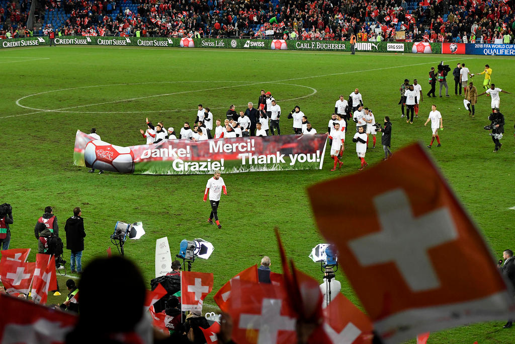 The Swiss fotball team stand behind a banner saying thankyou in various languages on the pitch