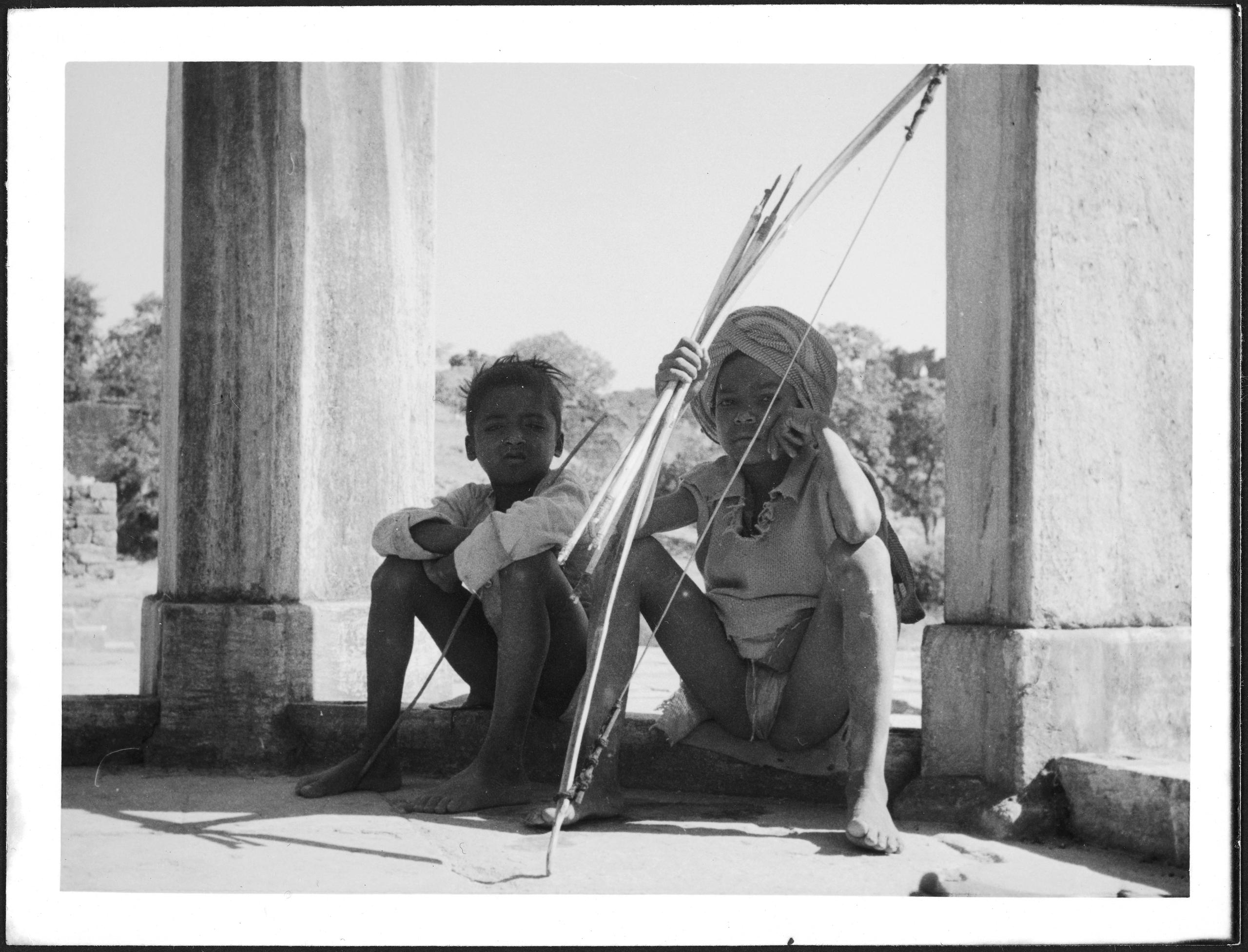 Dois garotos indianos com arco e flecha, sentados no chão