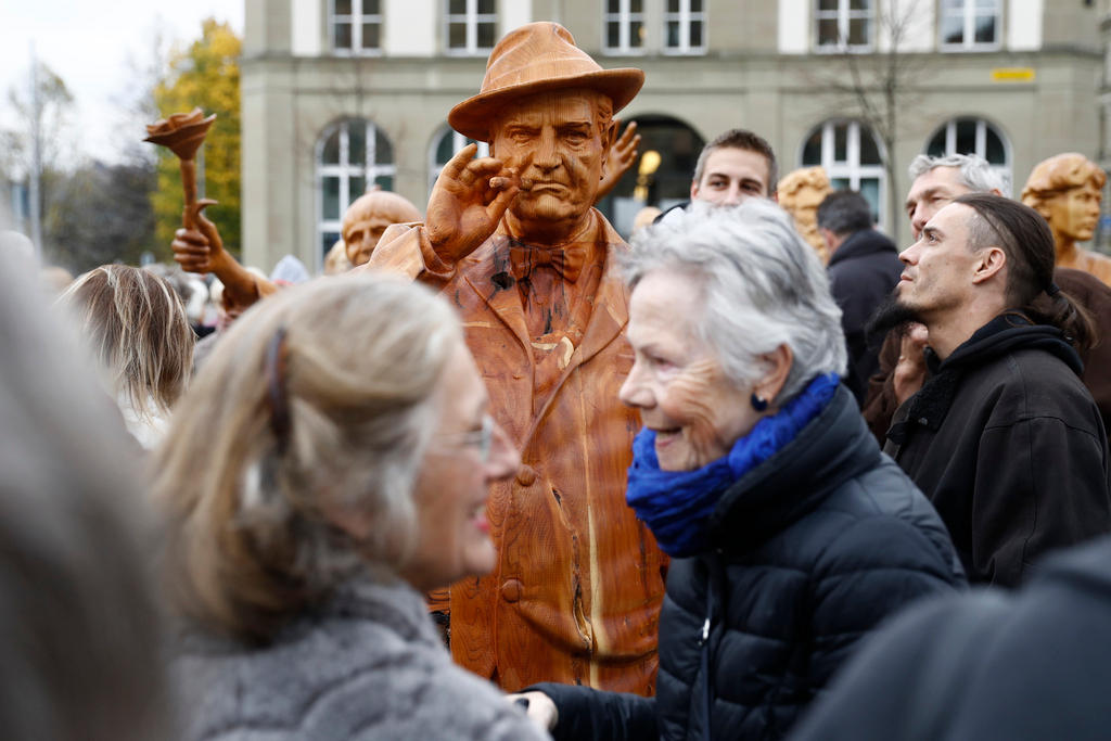 Una escultura de madera de Gottlieb Duttweiler expuesta en una plaza y circundada de personas que la contemplan