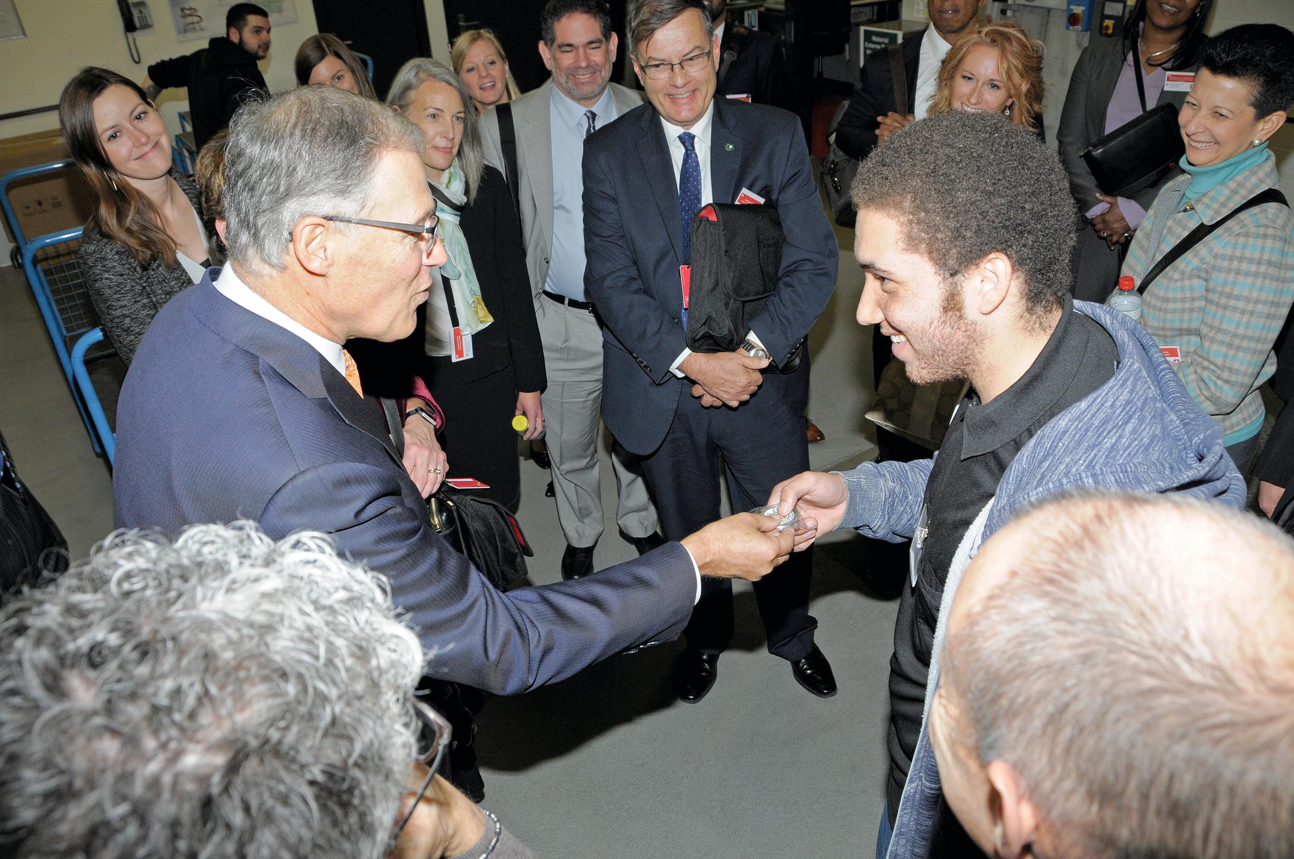 Washington Governor Jay Inslee presents an apprentice at Bern-based company CSL Behring with a gift from his home state