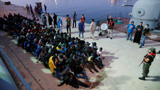 Eine Menschenmenge sitzt am Hafen