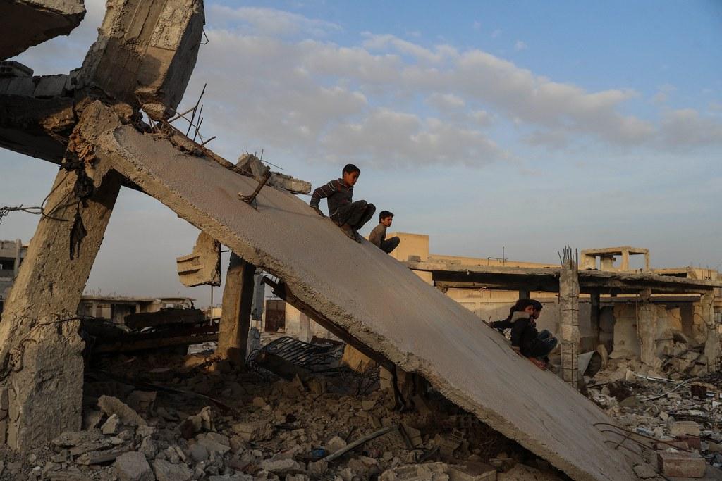 Children sit on the debris of a bombed building