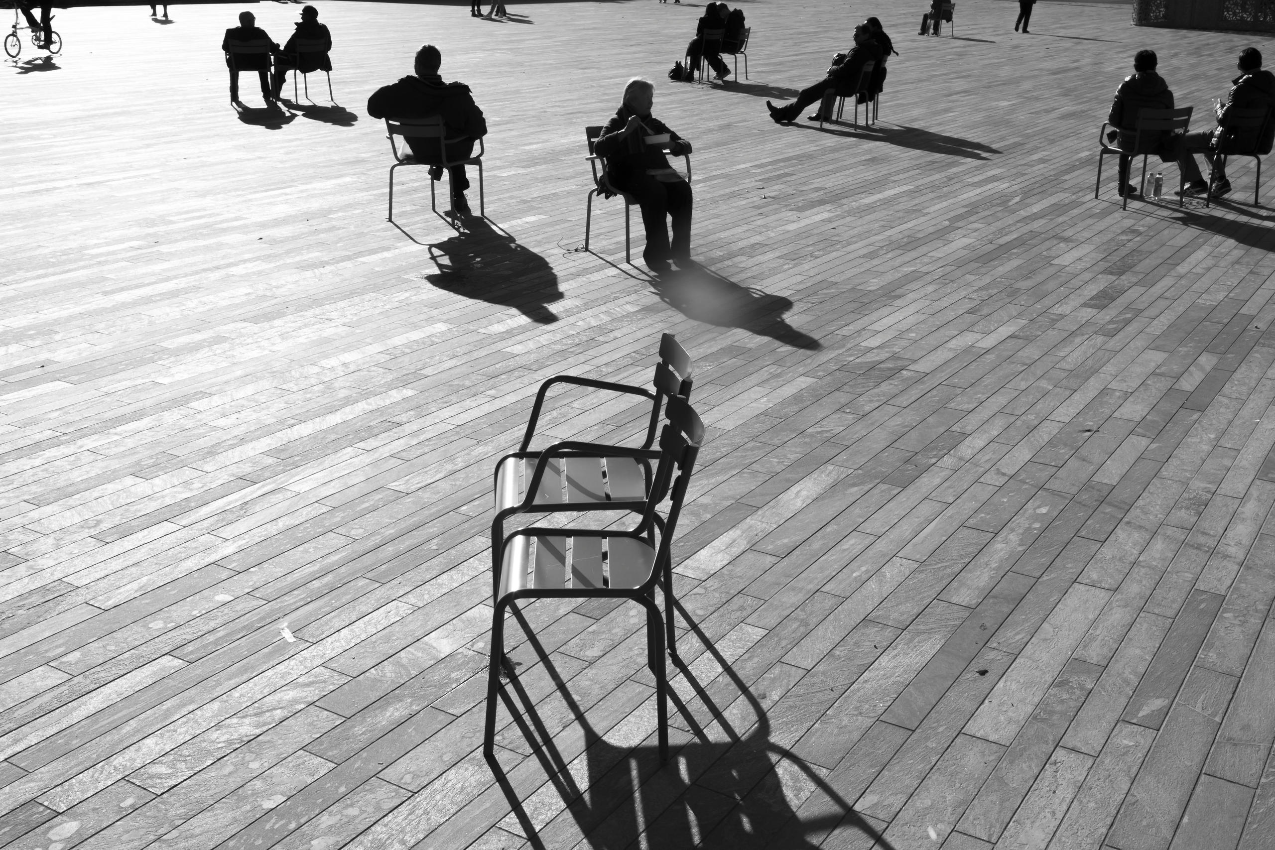 People sitting on scattered chairs on a public square