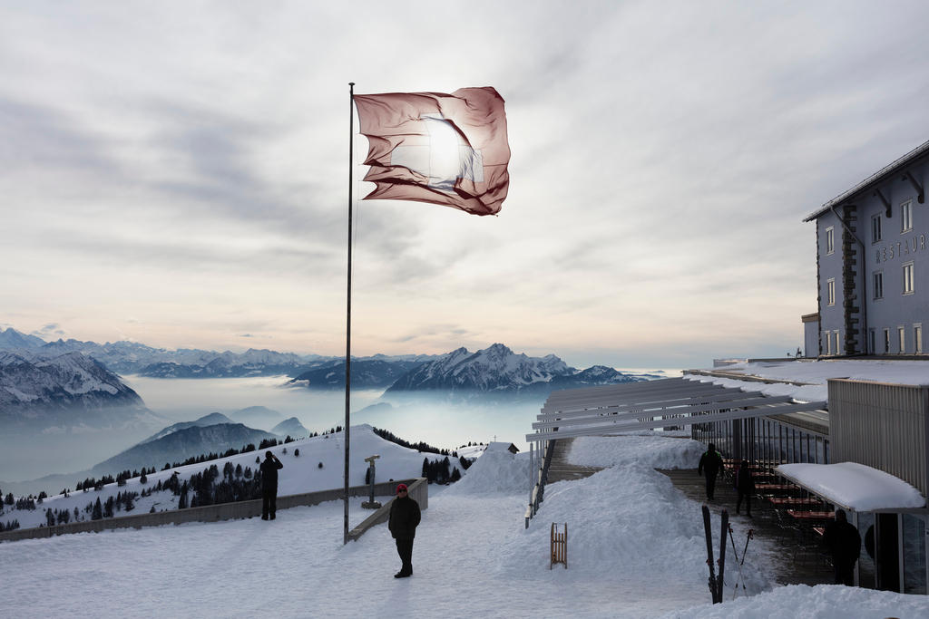 A Swiss flag blows in the wind on top of a snowy mountain peak