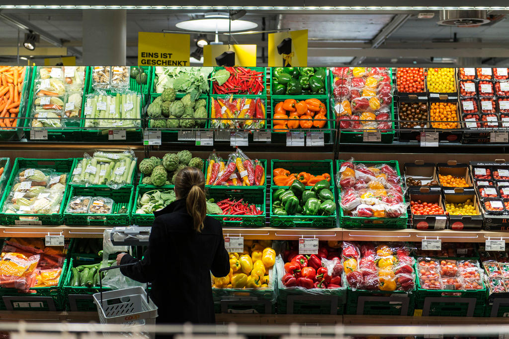 A woman stands before a grocery store s produce aisle