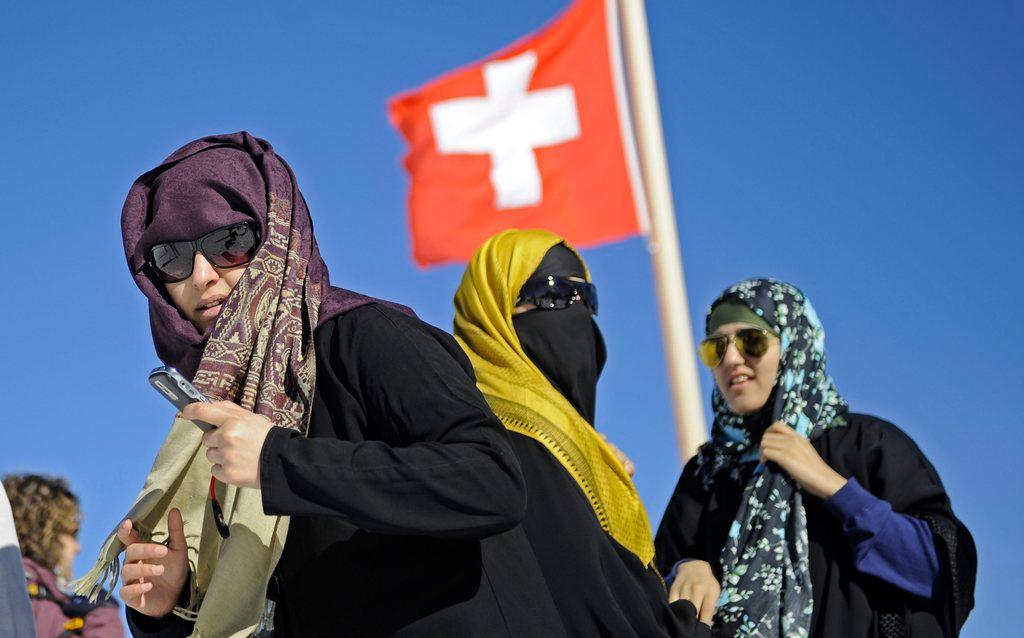 Three women wearing headscarves under a Swiss flag