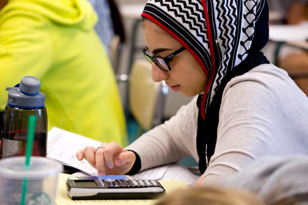 A girl wearing a headscarf uses a calculator