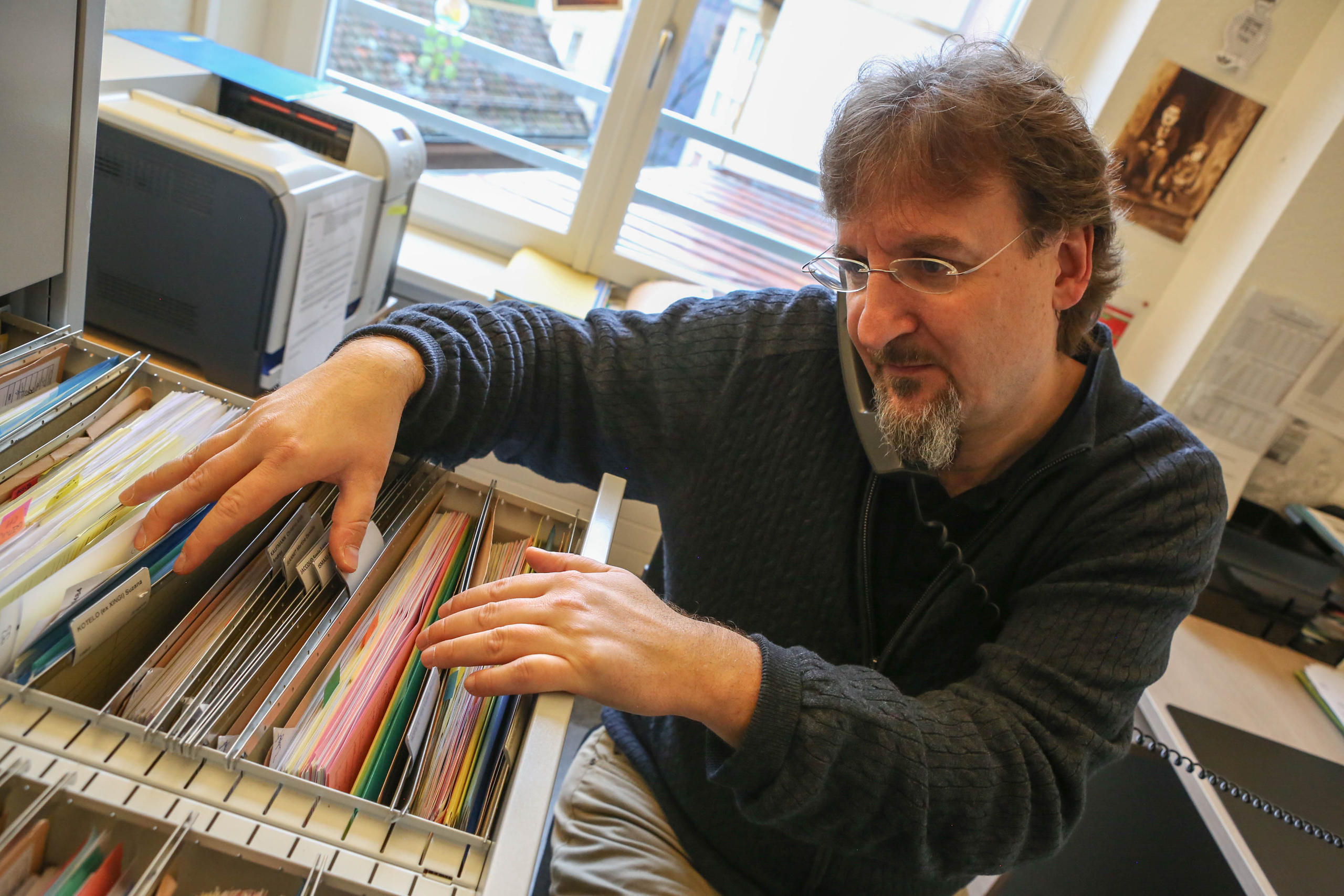 un uomo cerca un fascicolo nello schedario mentre è al telefono