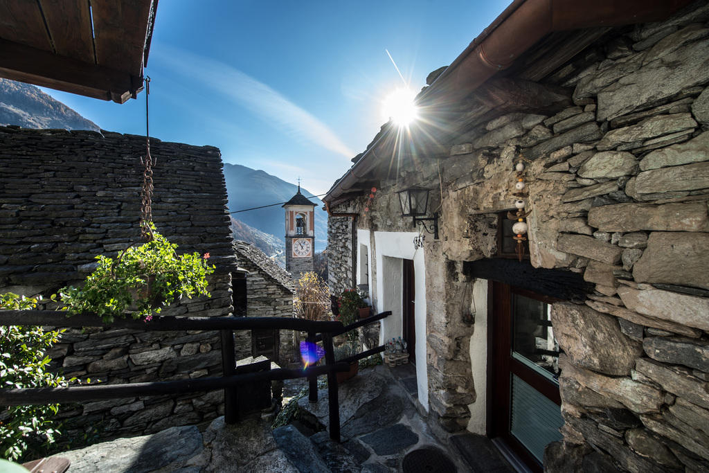 Image of stone buildings in the Swiss village of Corippo with a church tower in the background