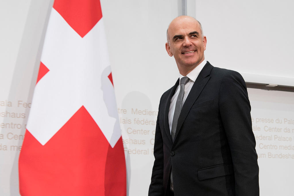 Alain Berset smiling besides a Swiss flag