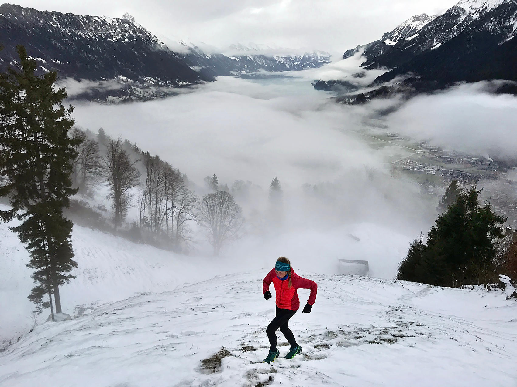 Runner running up snowy, wet slope with mist hanging above valley in background