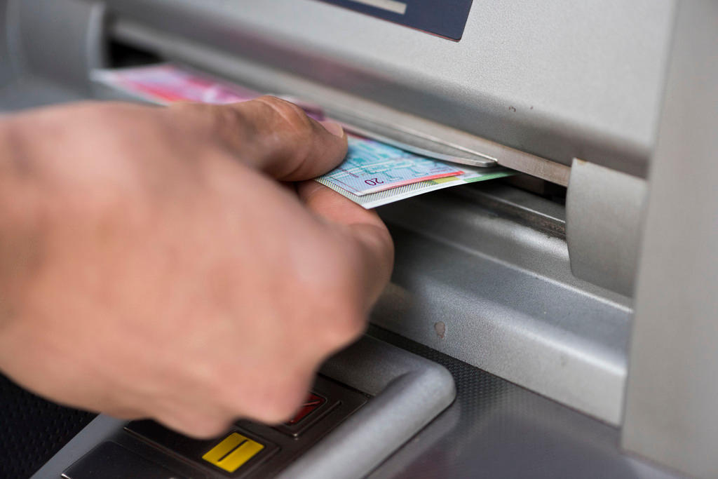 A person takes a Swiss banknote out of an ATM