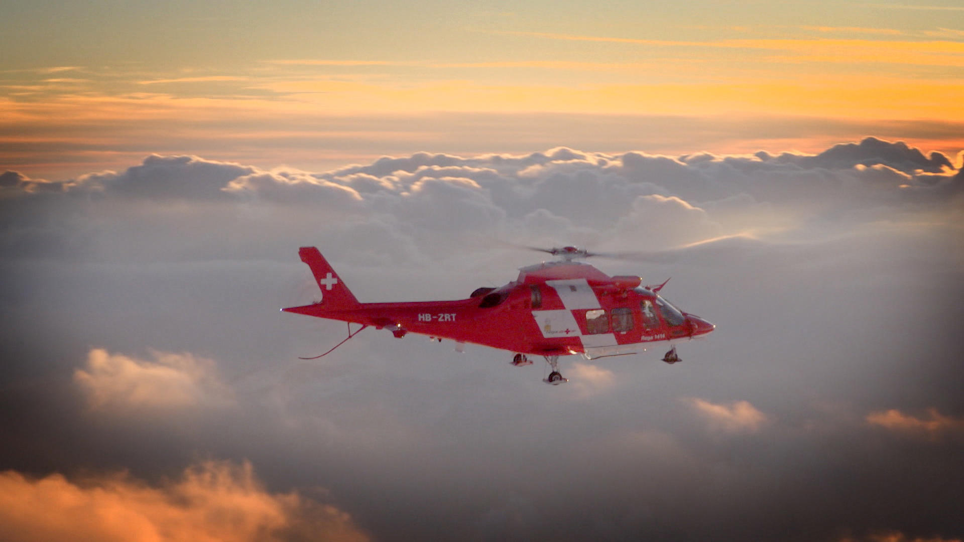 Rega helicopter in flight over clouds.