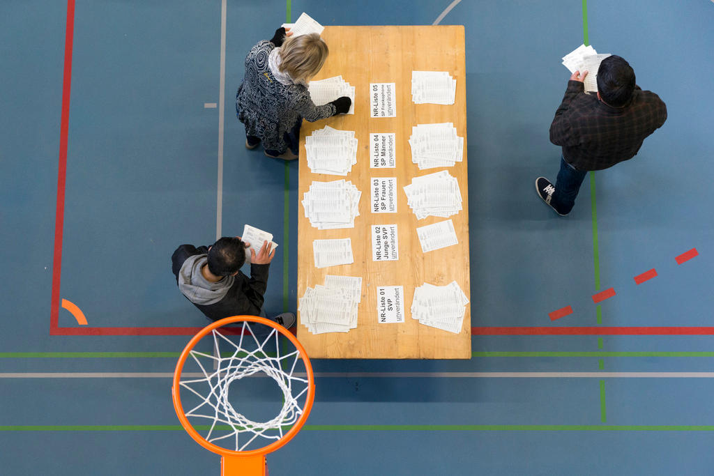 Ansicht von oben auf ein Pult mit Abstimmungszetteln und stehenden Menschen