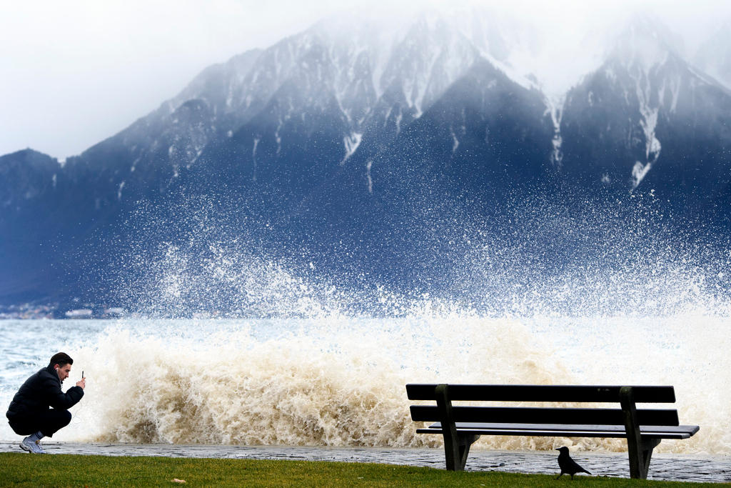 Un uomo accovacciato in riva al lago scatta una foto con un telefonino mentre la tempesta provoca onde impressionanti.