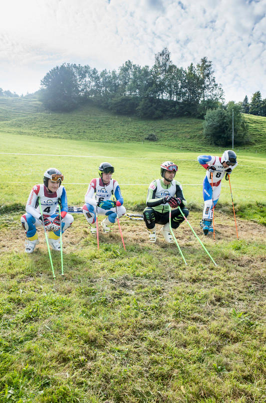 Vier Männer in Skiausrüstung sitzen auf einem Feld