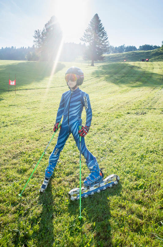 Kind auf Skiern auf Gras