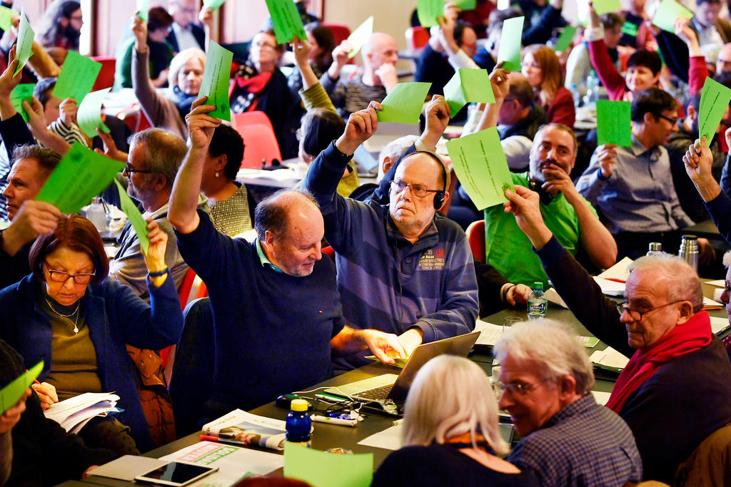 People at long tables holding their voting papers in the air