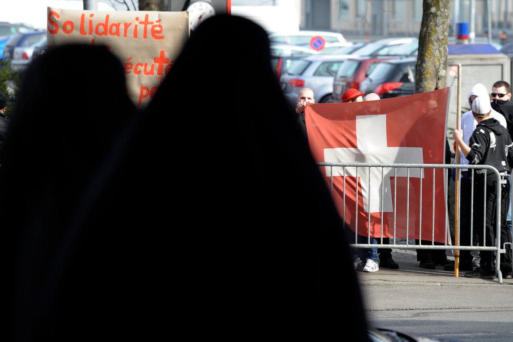 Duas mulheres vestindo burcas em frente a uma bandeira suíça