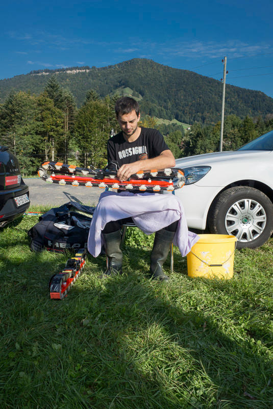 Junger Mann sitzt im Gras und schmiert Wachs auf einen Ski