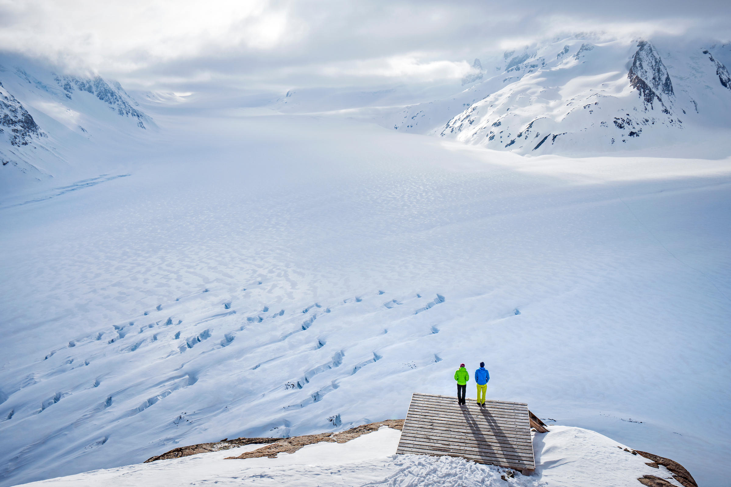 Two people at bottom of image look out onto Aletsch glacier