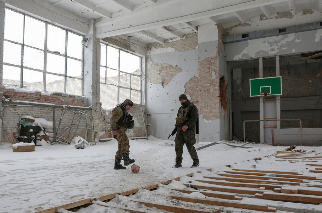 Zwei Soldaten spielen in einer verschneiten und beschädigten Halle mit einem Fussball.