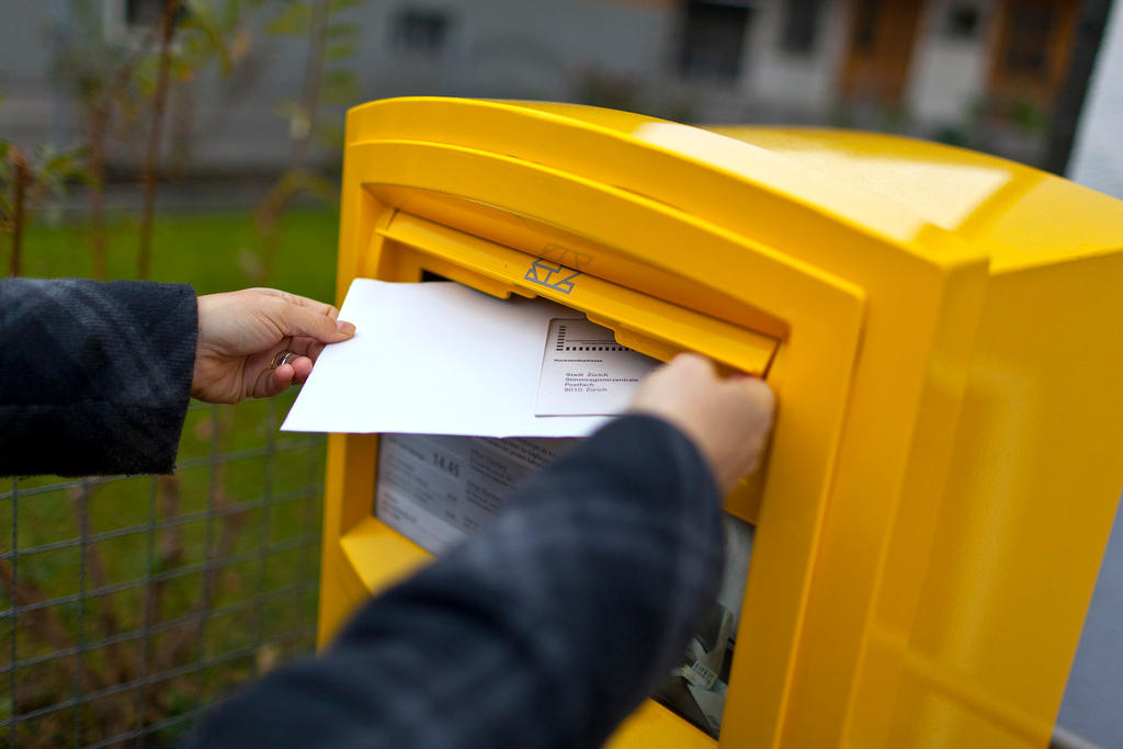 A woman drops an envelope with her vote-by-mail ballot in a letterbox