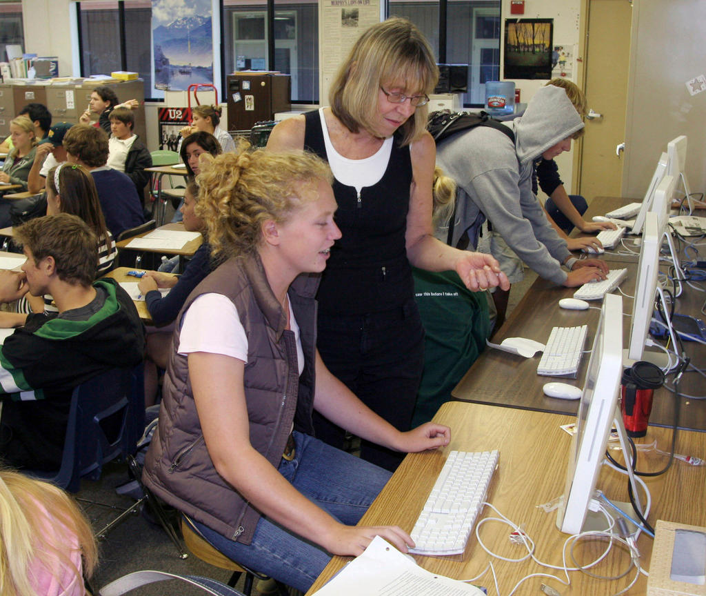 Una estudiante frente a su computadora y su maestra al lado