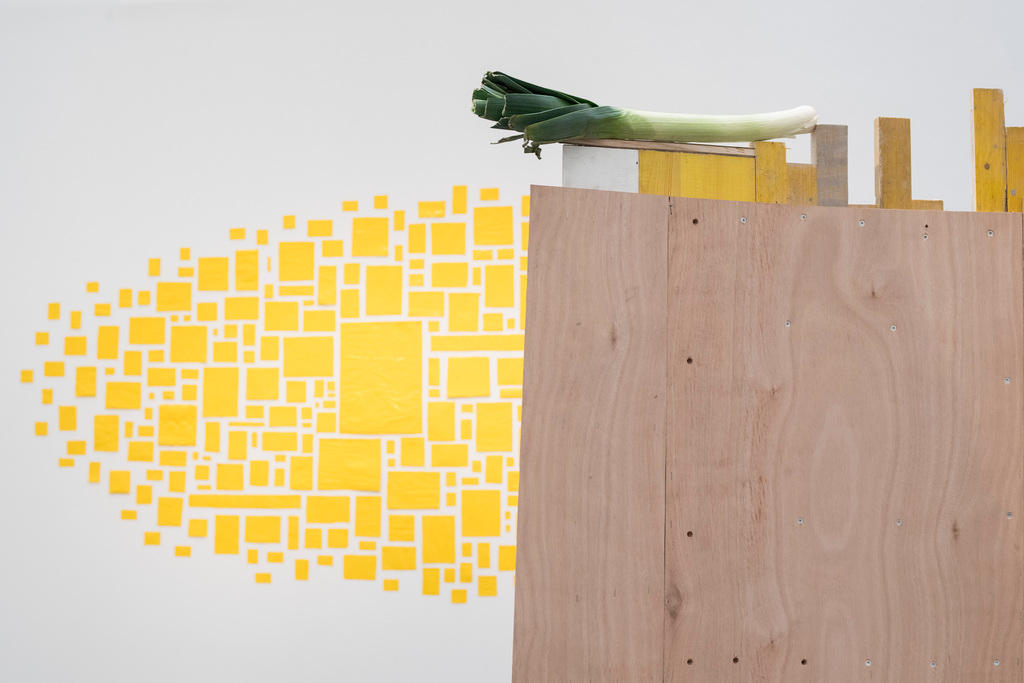 Kunstwerk vor gelbem Hintergrund, Lauch auf Holzskulptur