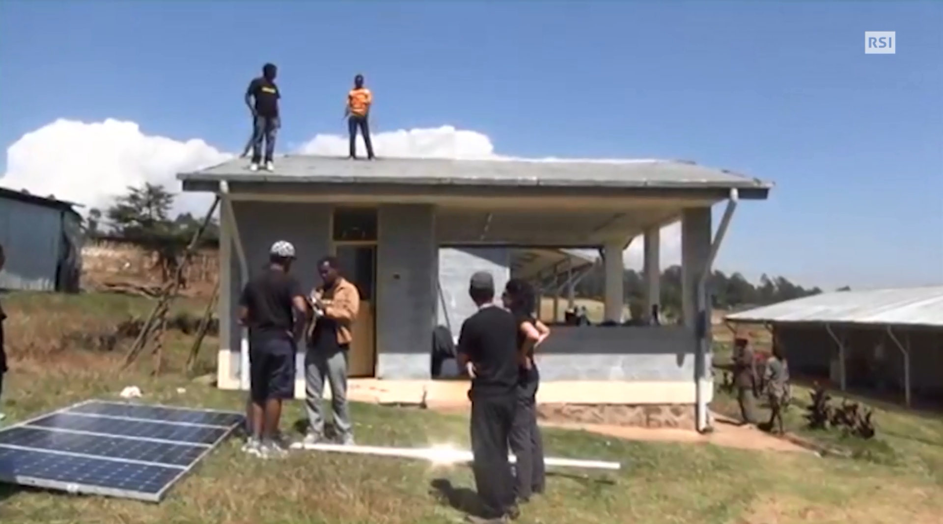Quattro operai e due supervisori installano un impianto fotovoltaico su un piccolo edificio in Afria.
