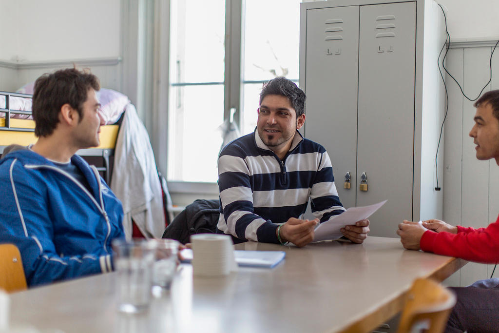 Three men sit at a table at the asylum center Gutshof in canton Bern