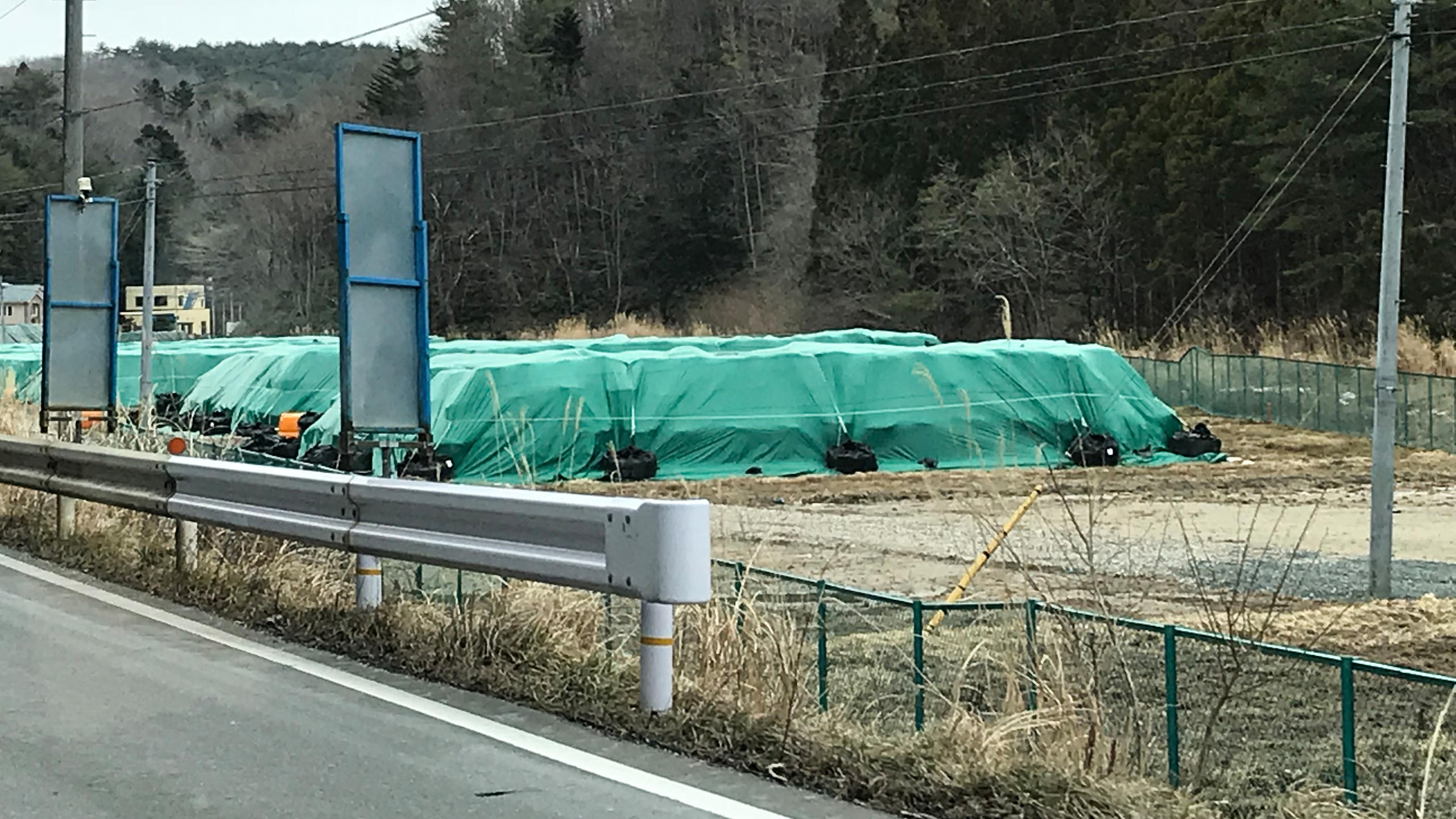 Green plastic sheeting covers rows of contaminated soil along the National Highway 6