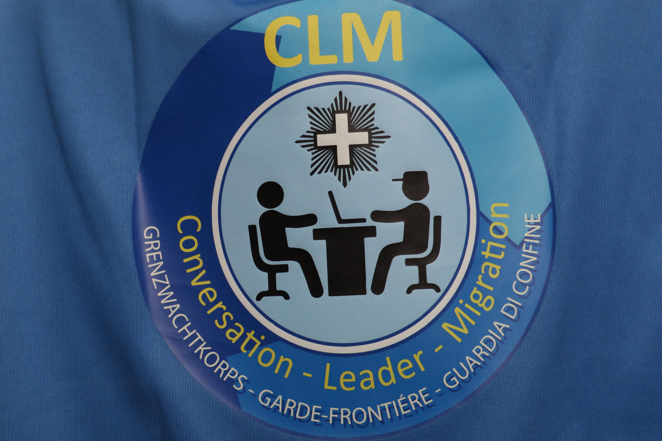 Logo dei CLM (personale specializzato che intervista i migranti) ritratto in primo piano sulla mantellina che indossano