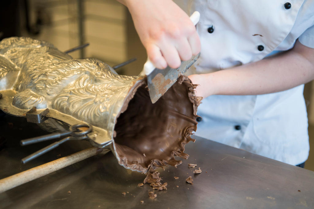A funcionária raspa o chocolate em excesso na forma.