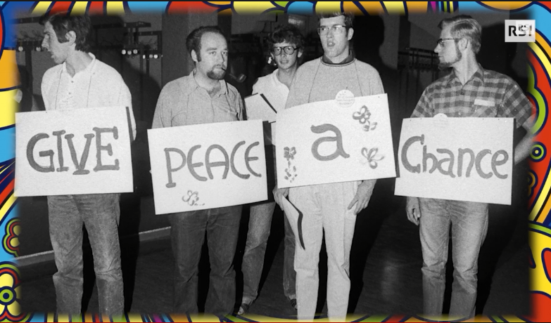 quattro uomini tengono un cartellone su cui c è scritto give peace a chance
