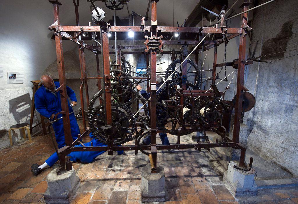Two men in blue overalls attend to the clockwork inside the Zyglogge tower in Bern, Switzerland.